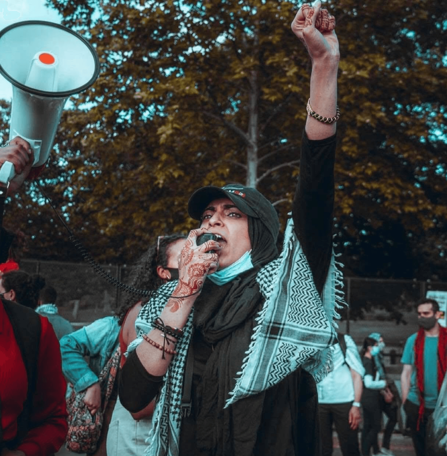 Maheen Haq speaking into a microphone with her fist raised at a Palestine protest